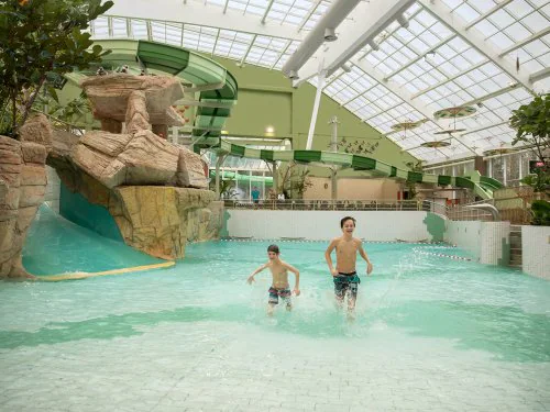 Een foto van het indoor waterpretpark aqua mundo Ardennes. Twee jongens zijn aan het spelen in het zwembad met op de achtergrond meerdere glijbanen.