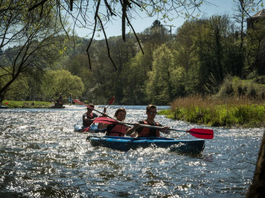 Twee kayak bootjes die peddelen over een wilde rivier, De kayakers zelf lachen en hebben een reddingsvest aan.