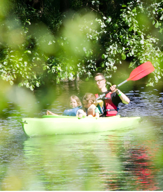 Een foto van een man met twee kindjes die kayakt over het rustige water.