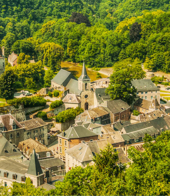 Een luchtfoto van de gemeente Rendeux, bestaande uit verschillende huizen en een kerk. Allemaal gebouwt in baksteen en omringt door groene bomen